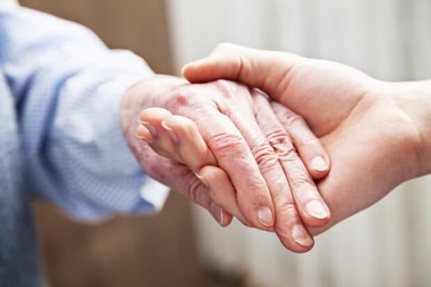 A carer gently holding an older person's hand